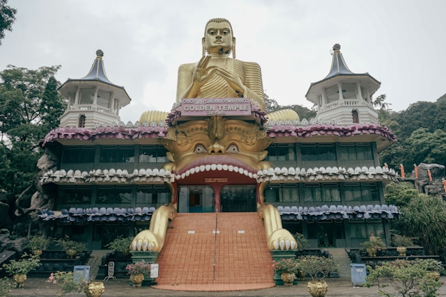 A large golden Buddha statue sitting in front of a building in Sri Lanka. Photo by photographer via Unsplash (https://unsplash.com/photos/a-large-golden-buddha-statue-sitting-in-front-of-a-building-IS5LfDPkTDg)